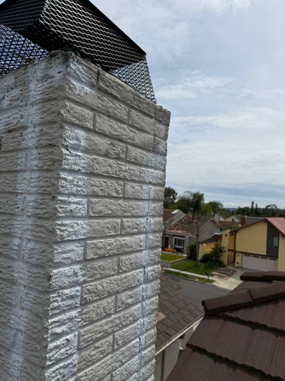 Restored California chimney corner after California Airduct Pros tuckpointing — smooth painted brick finish, crack eliminated, new stainless cap visible